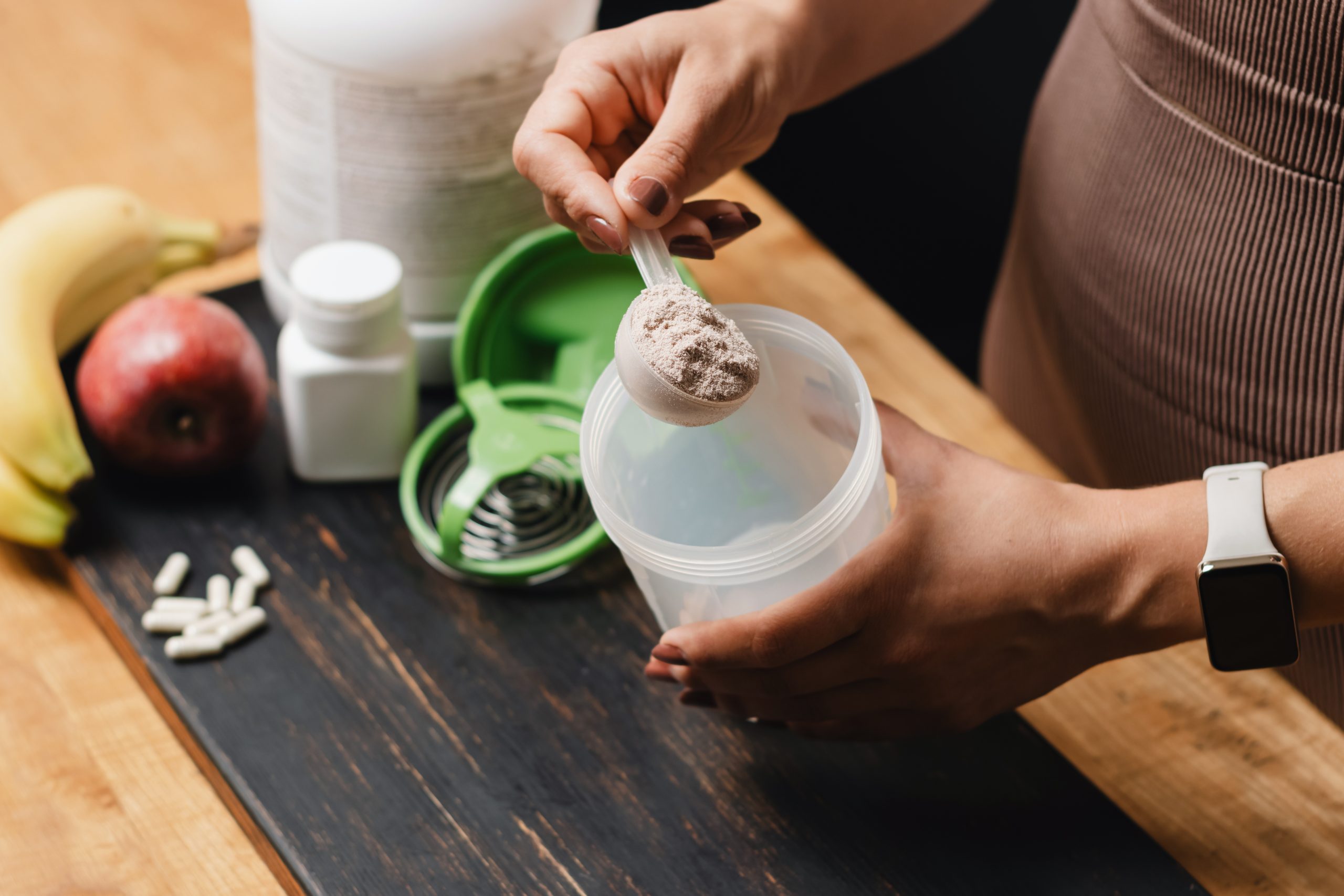 Mulher colocando whey protein em um copo.